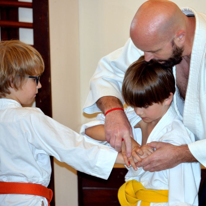 Oktató segíti az alsós gyerekek önvédelmi technikáinak gyakorlását aikido edzésen