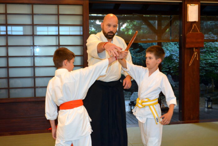 Dr. Havasi Tamás vezető oktató két gyermek fegyveres aikidogyakorlatát segíti az esztergomi Tada Ima Aikido Dojóban.